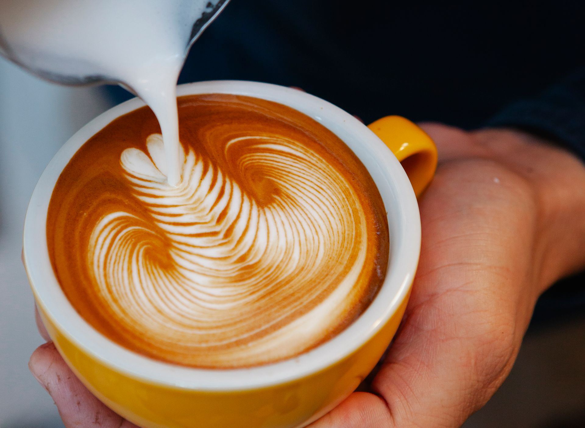 Barista pouring latte art from a milk jug
